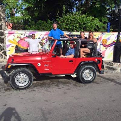 Red Jeep with four people parked near a colorful mural.