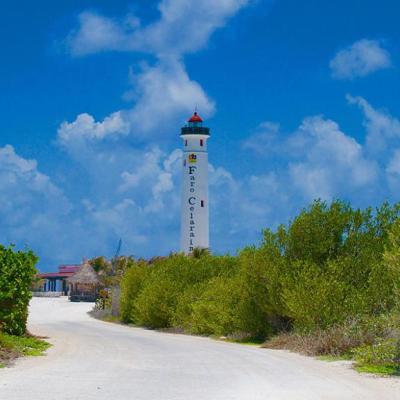 Lighthouse with 'Faro Celarain' sign, surrounded by greenery, under a clear blue sky.