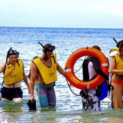 Group in yellow vests and snorkels wading in shallow sea with life ring.
