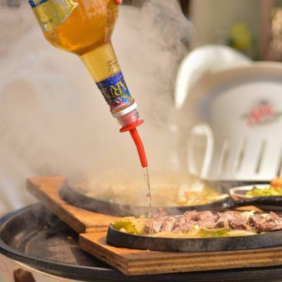 Tequila bottle pouring onto sizzling fajita platter with steam rising.