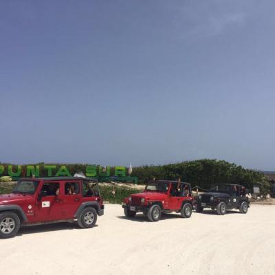 Three jeeps parked in front of 'Punta Sur' sign on a sandy area.
