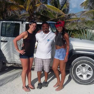 Three people posing in front of a white jeep on a tropical beach.