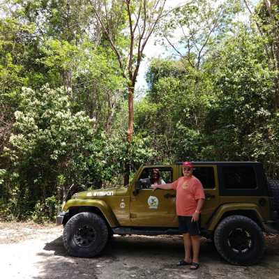 Person standing by a yellow Jeep in a forested area.