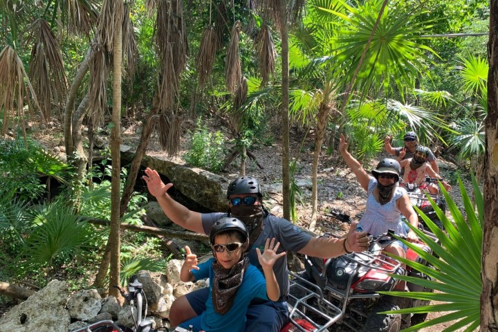 People riding ATVs through a tropical forest with helmets and bandanas.