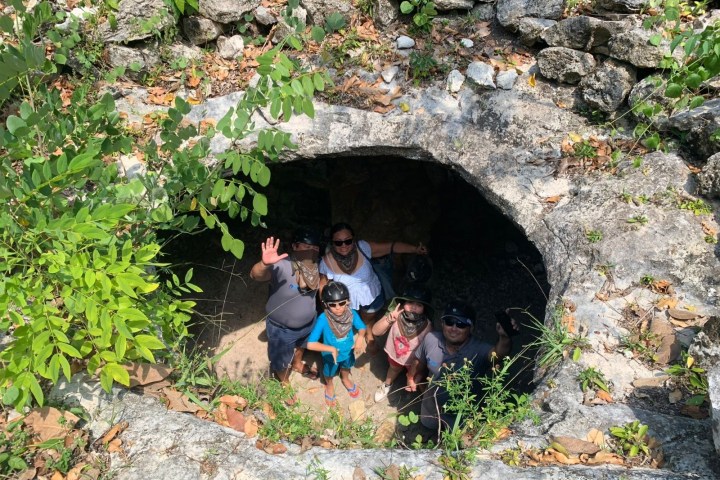 Group of people looking up from a rocky hole surrounded by plants.