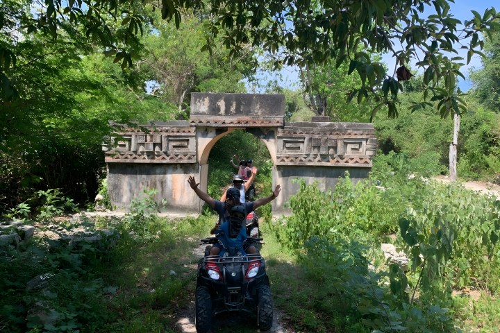 ATVs driving through an ancient stone arch surrounded by greenery.
