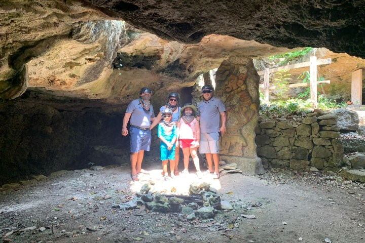 Group of five posing inside a cave with helmets and a Mayan mural.