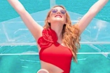 Person in red swimsuit joyfully poses on a yacht with turquoise water backdrop.
