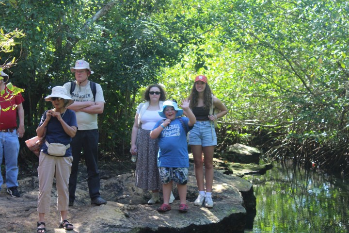 Group of people standing on a rocky path in a forested area near water.