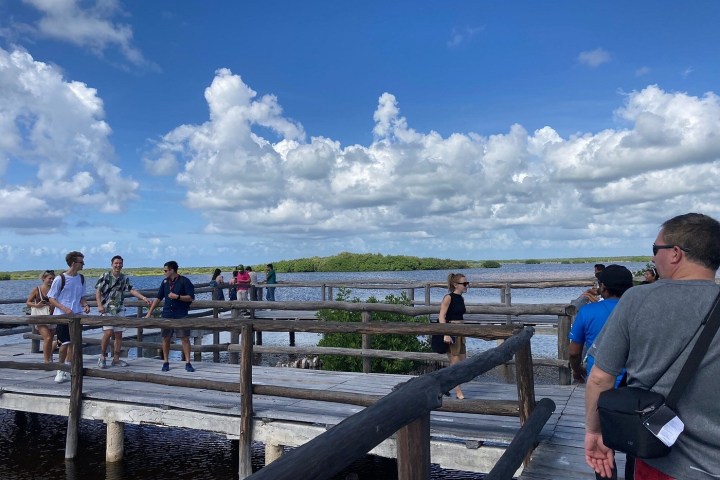 People walking on a wooden boardwalk over water under a blue sky with clouds.