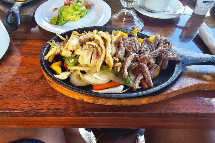 Sizzling fajita platter with beef, chicken, peppers, and onions on a wooden table.